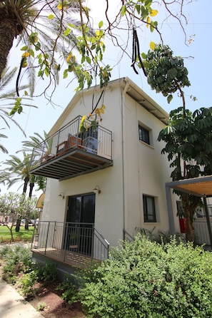 A two-story building with a balcony, surrounded by greenery and palm trees. - Kibbutz Ashdot Yaacov Ichud Country Lodging (Emek HaYarden)