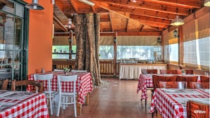 A restaurant with wooden ceiling beams, red and white checkered tablecloths, and a large tree trunk in the center. - Kibbutz Ashdot Yaacov Ichud Country Lodging (Emek HaYarden)