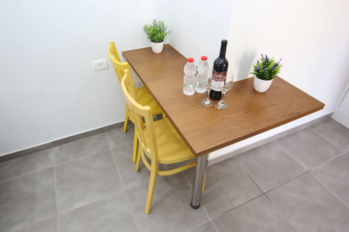 A small dining area with a wooden table, two chairs, and two potted plants.