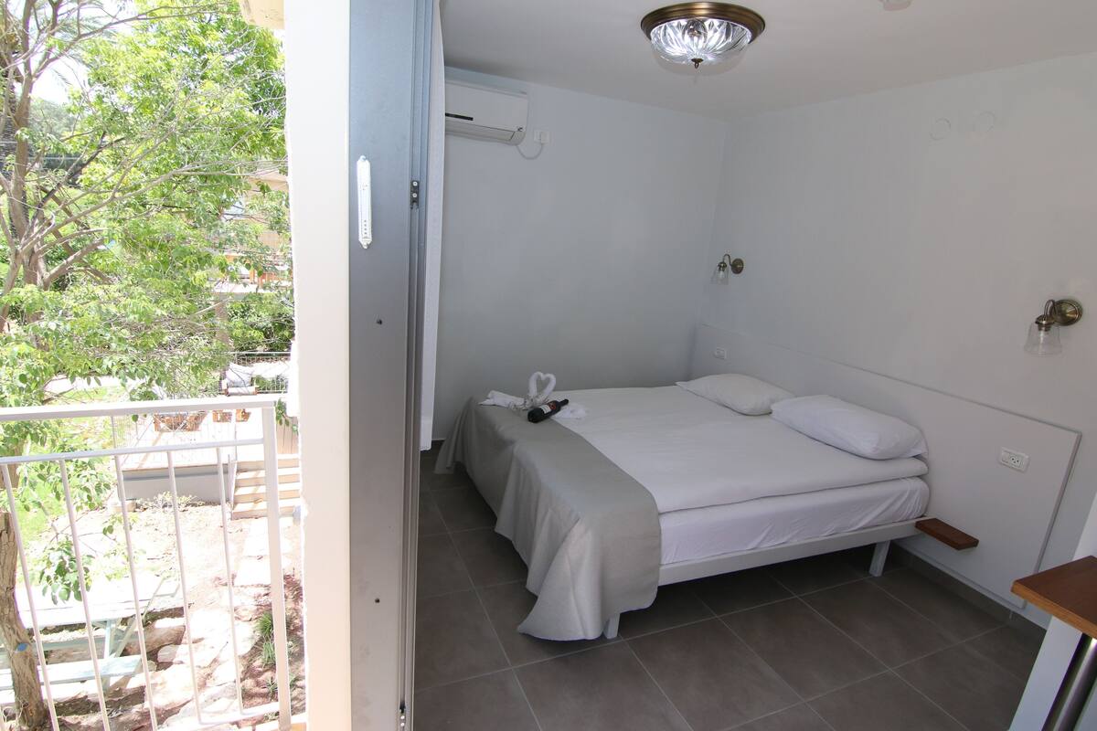 A bedroom with a bed, a bedside table, and a view of the outdoors.