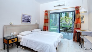 A bedroom with a bed, a desk, a chair, and a view of the garden through a glass door. - Kibbutz Ashdot Yaacov Ichud Country Lodging (Emek HaYarden)