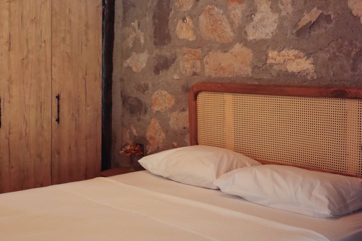 Une chambre avec un mur en pierre, une armoire en bois et un lit avec une literie blanche.
