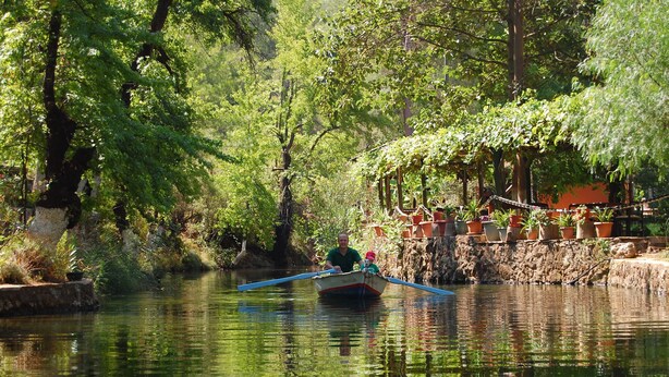 Una barca en un río tranquilo rodeada de exuberante vegetación y un muro de piedra con macetas.