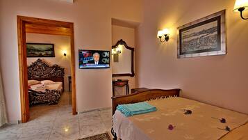 A bedroom with a bed, a television, a painting, and a lamp.