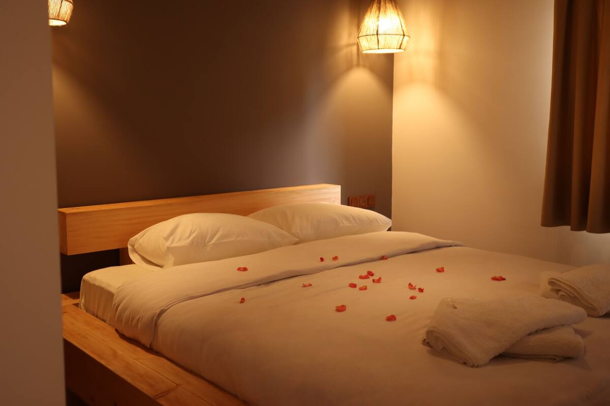 Un lit parfaitement fait, avec des draps blancs et des pétales de rose éparpillés sur le couvre-lit.