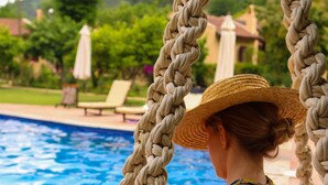 Una persona sentada en un columpio de cuerda al lado de una piscina, con vistas despejadas a la piscina y follaje en el fondo.