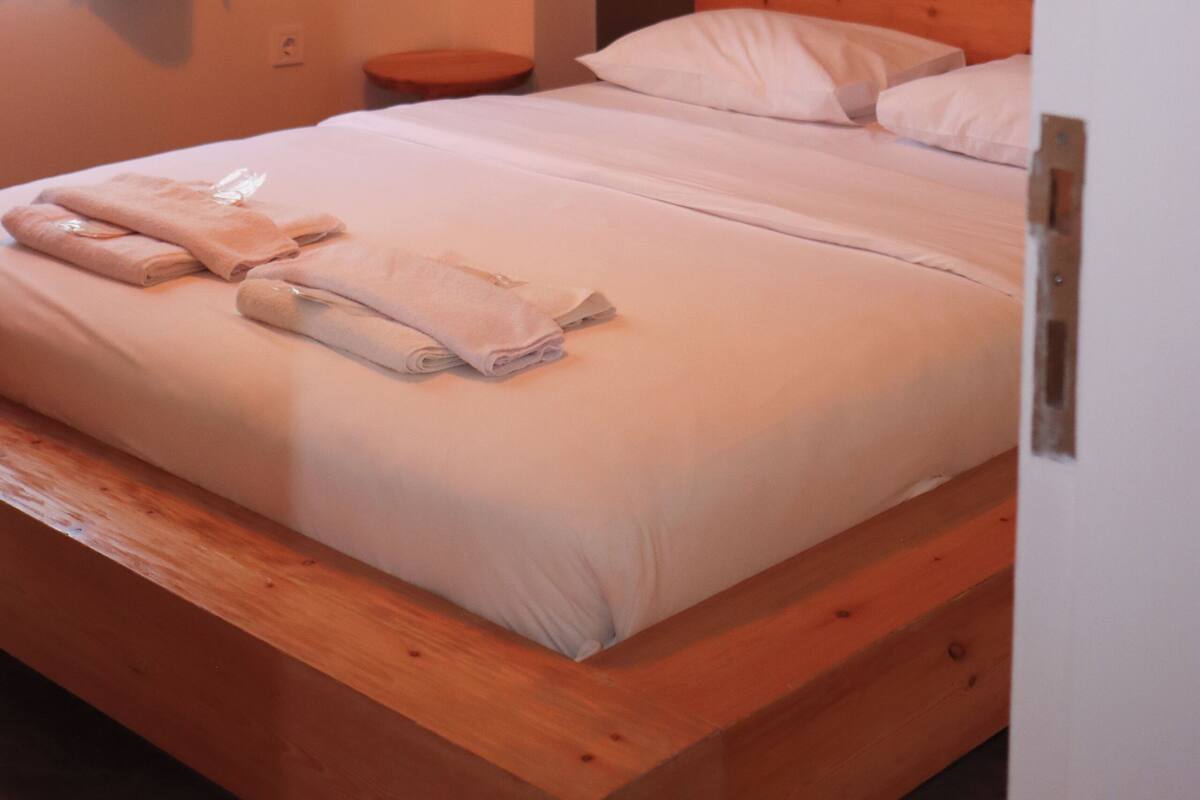 Une chambre à coucher avec un cadre de lit en bois, une table de chevet, un appareil de climatisation et un luminaire suspendu.