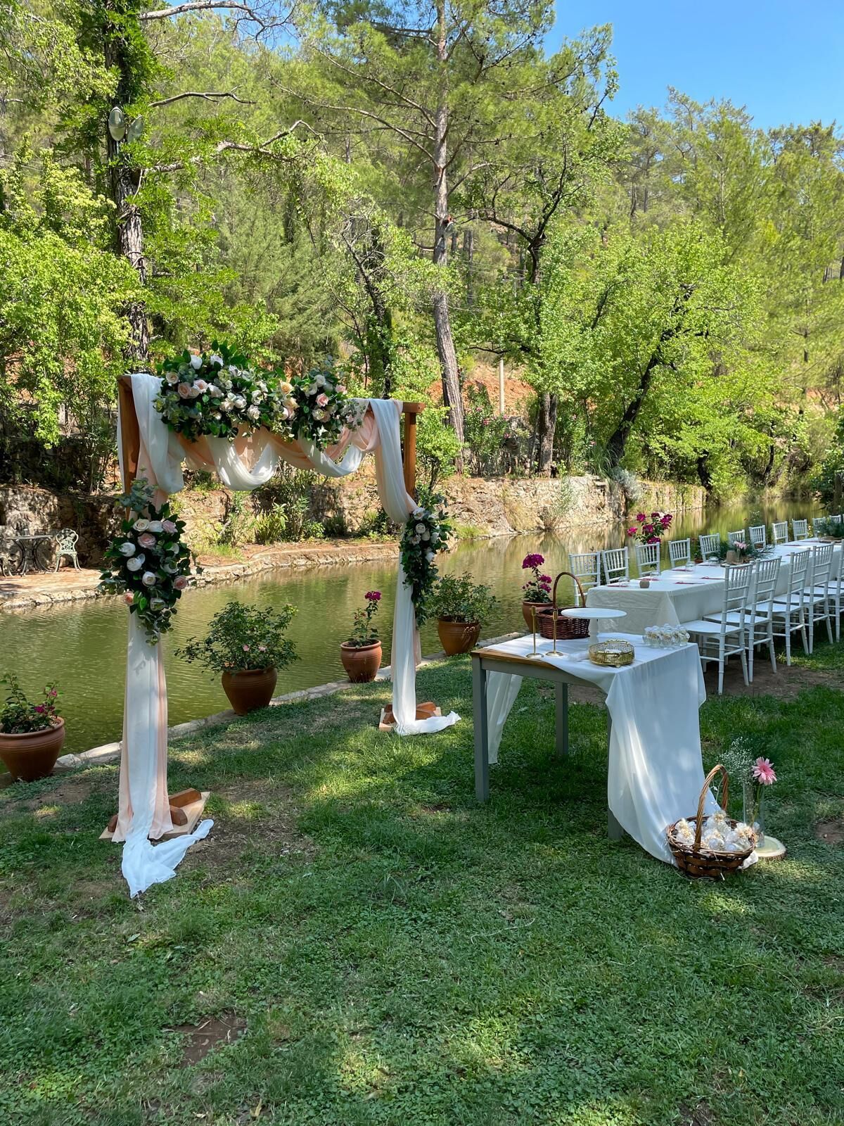 An outdoor wedding setup with a decorated arch, a table with chairs, and potted plants.