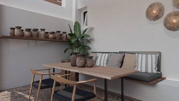 A modern dining area with a wooden table and chairs, a potted plant, and a sofa with cushions.