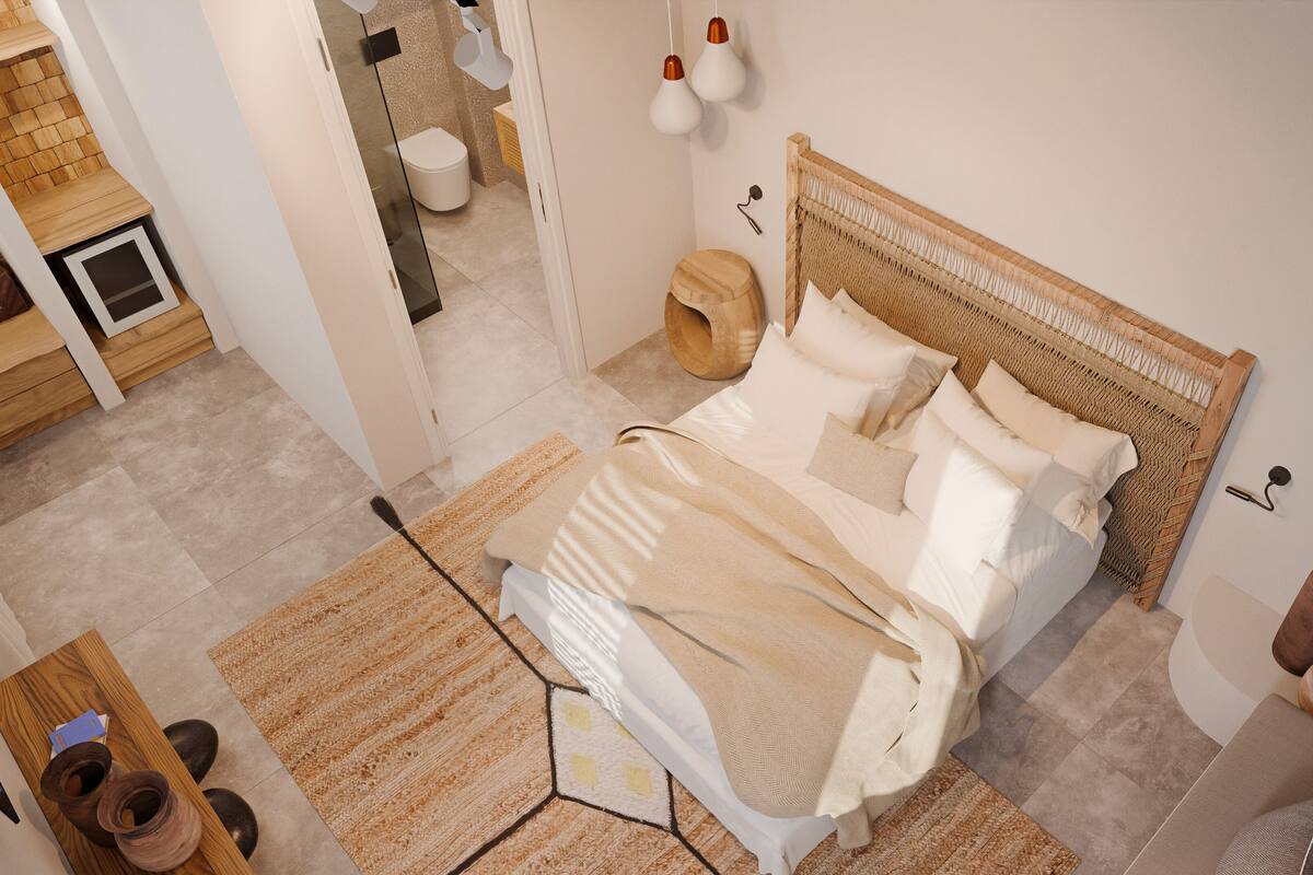 Un dormitorio moderno con cabecera de madera, una cama grande con muchas almohadas, una mesita de noche con lámpara y vista al baño.
