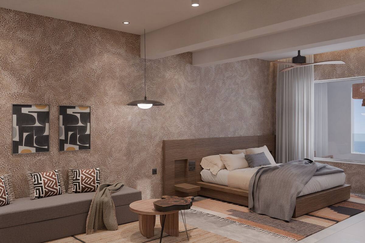 Un dormitorio moderno con pared texturizada, una cama con muchos cojines, una mesita redonda y vista al mar a través de una ventana.
