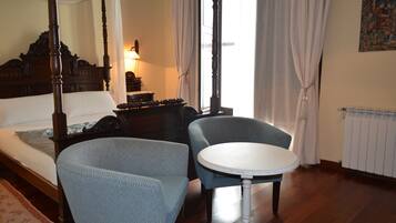Una cama con dosel y tablero de madera, una mesa redonda con superficie blanca y dos sillones tapizados.