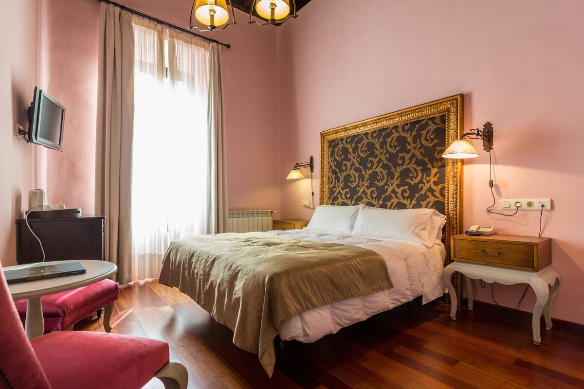 A hotel room with a bed, bedside table, lamp, chair, desk, and a television.