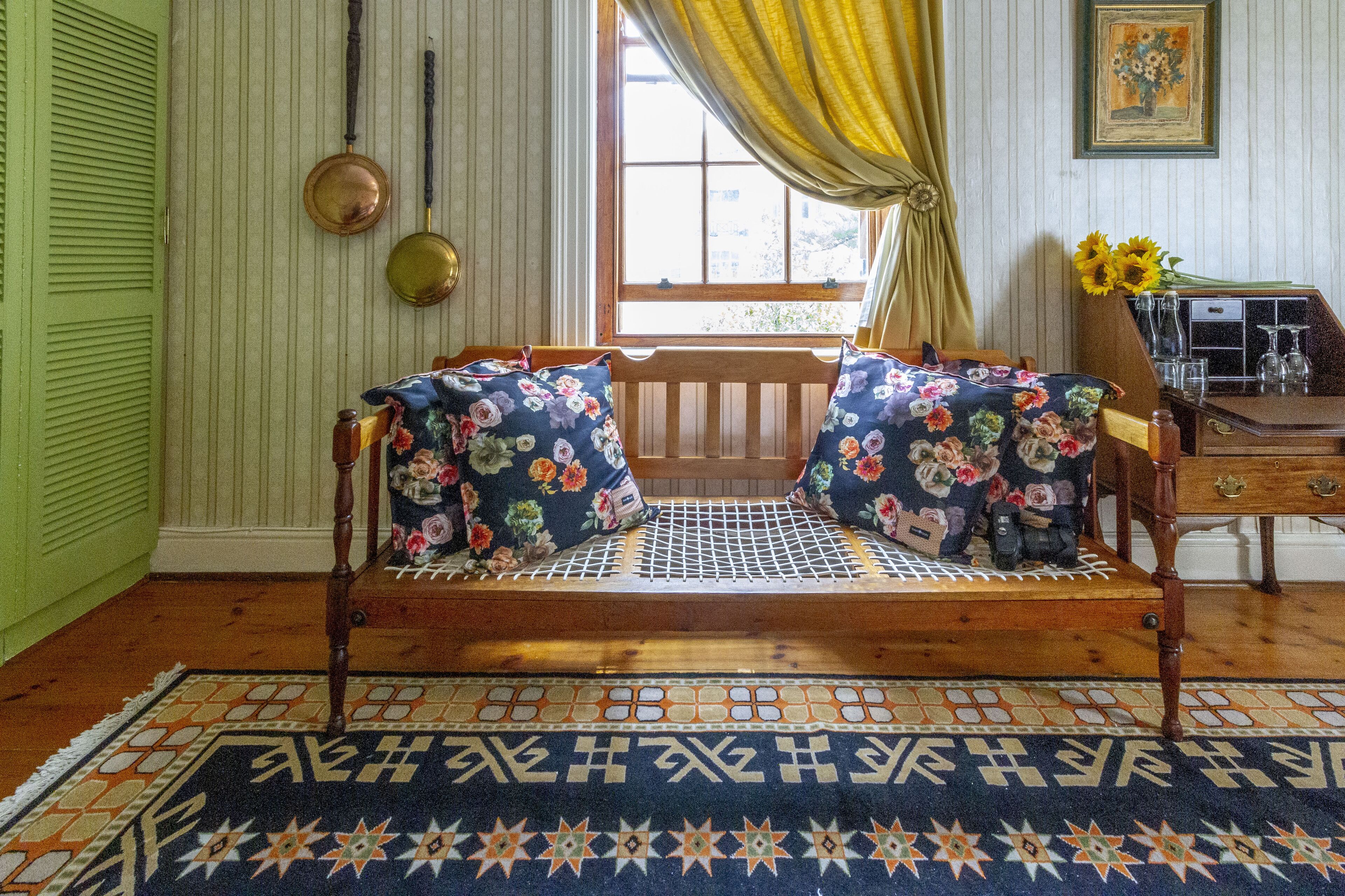 A wooden bench with floral cushions, a patterned rug, and a window with curtains.