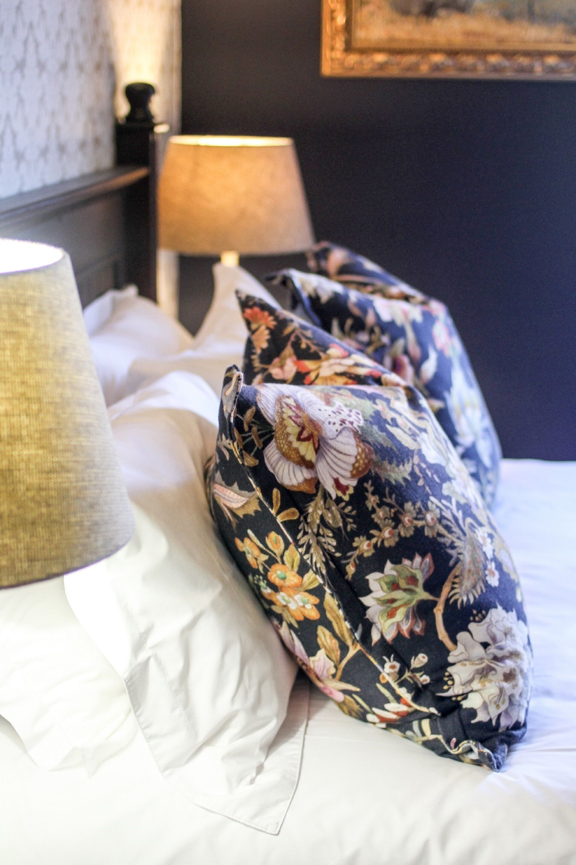 Una cama bien hecha con almohadas estampadas con motivos florales y una lámpara al lado.