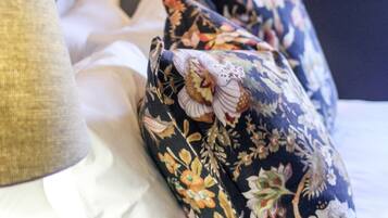 Una cama bien hecha con almohadas estampadas con motivos florales y una lámpara al lado.