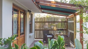Un patio techado con pérgola de madera, una silla de mimbre y una mesa.