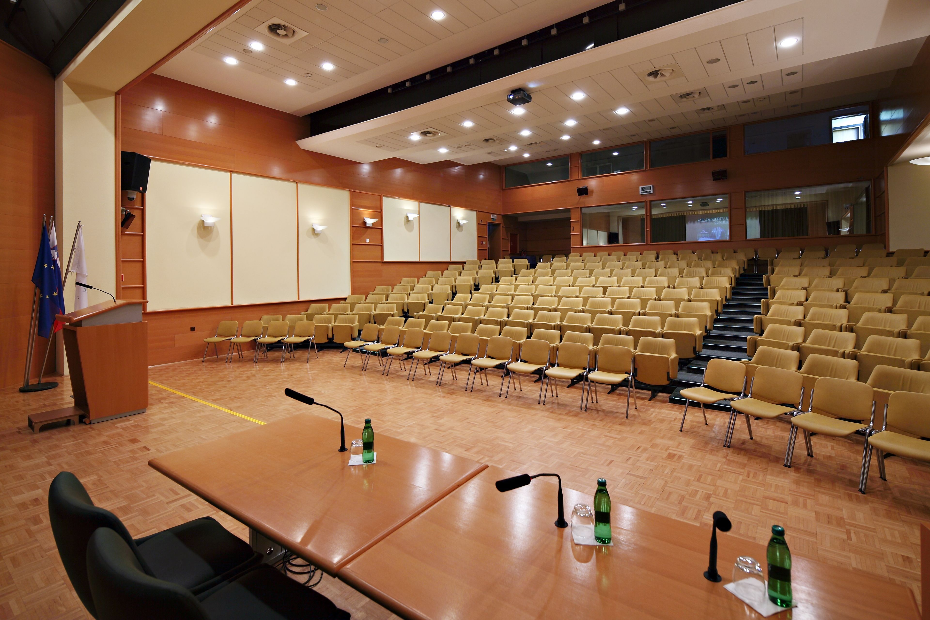 Konferenssisali, jossa on riveissä tuoleja, puhujapönttö ja projektorikangas.