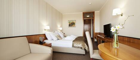 A hotel room with a bed, a sofa, a desk, and a television.