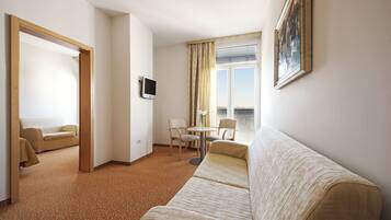 Habitación de hotel con sofá, una pequeña mesa con sillas, televisor y ventana con cortinas.