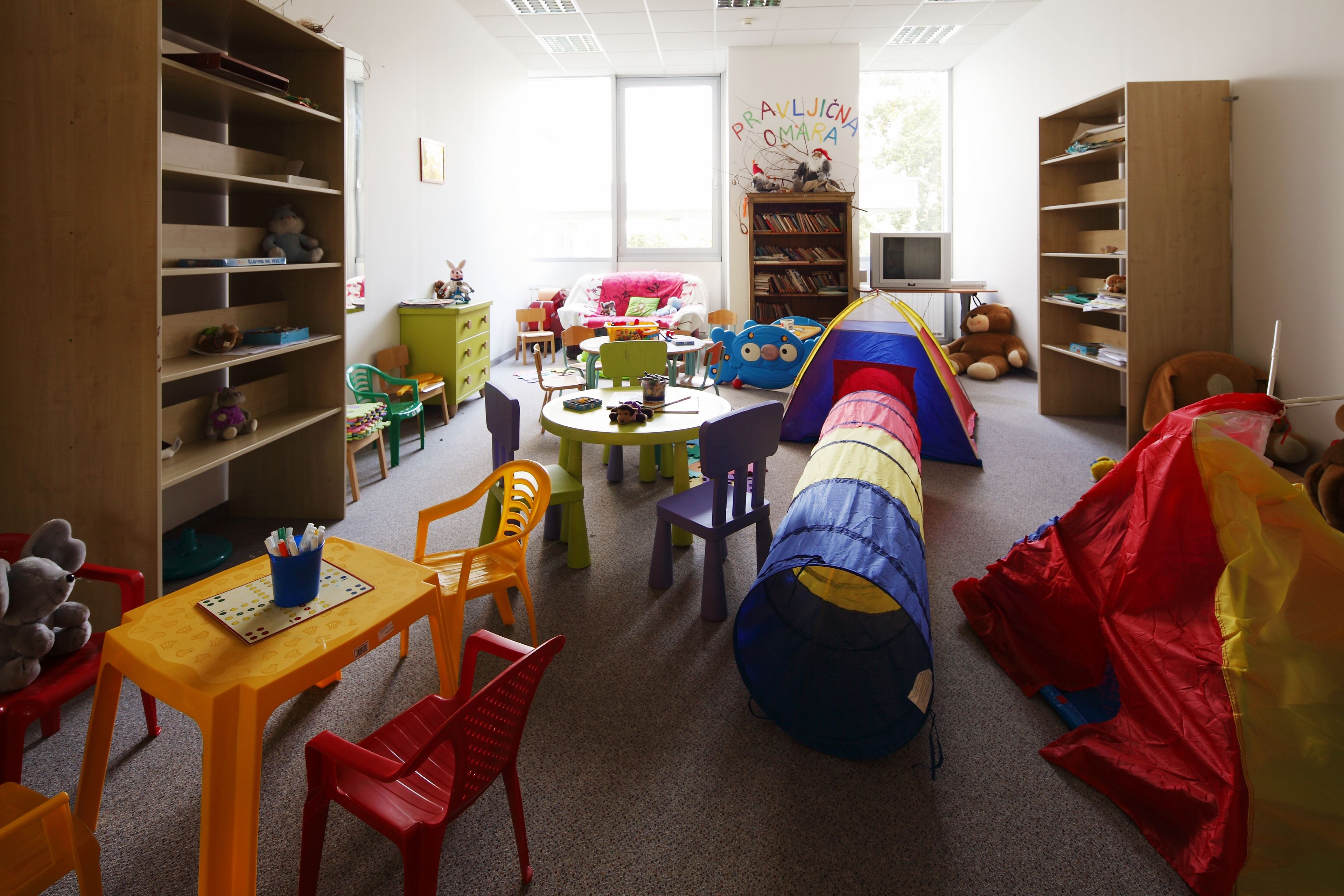 Una sala de juegos infantil con muebles coloridos, una carpa de juegos y una estantería.