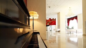 Ein Flügel in einer geräumigen, hell erleuchteten Lobby mit einem Chandelier und roten Vorhängen.