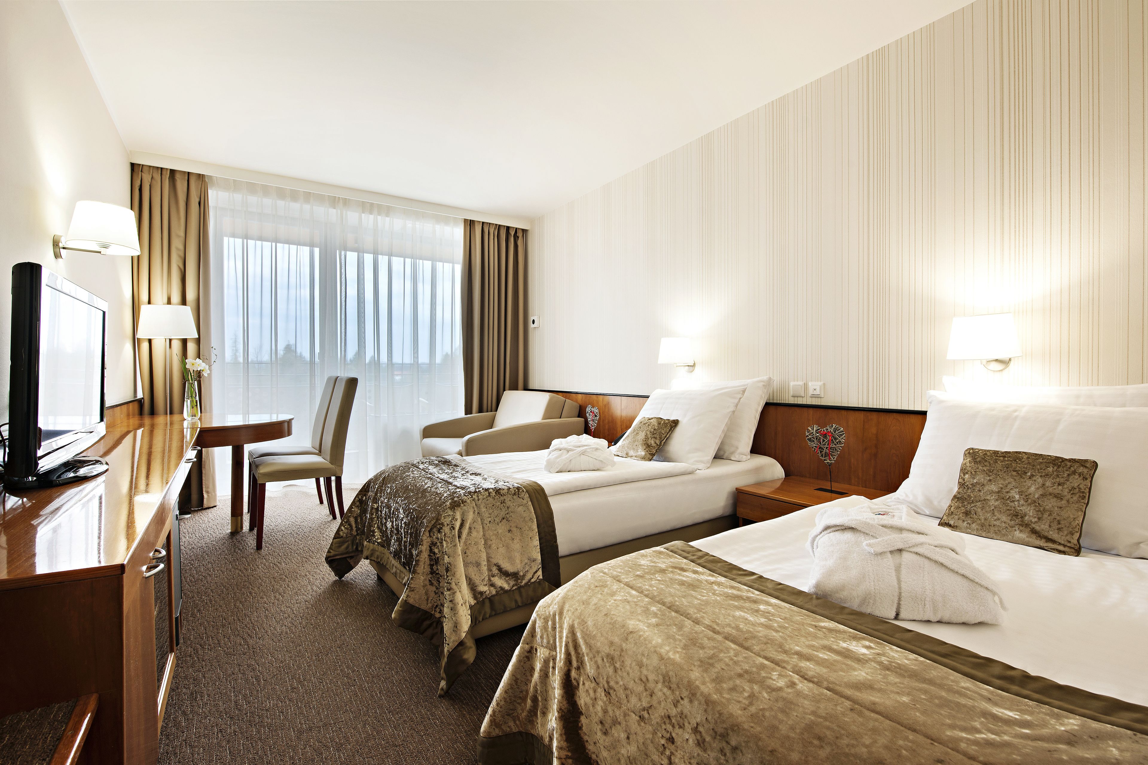 A hotel room with two beds, a desk, a chair, and a television.