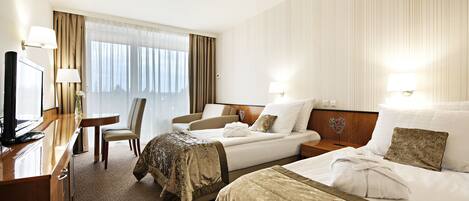 A hotel room with two beds, a desk, a chair, and a television.