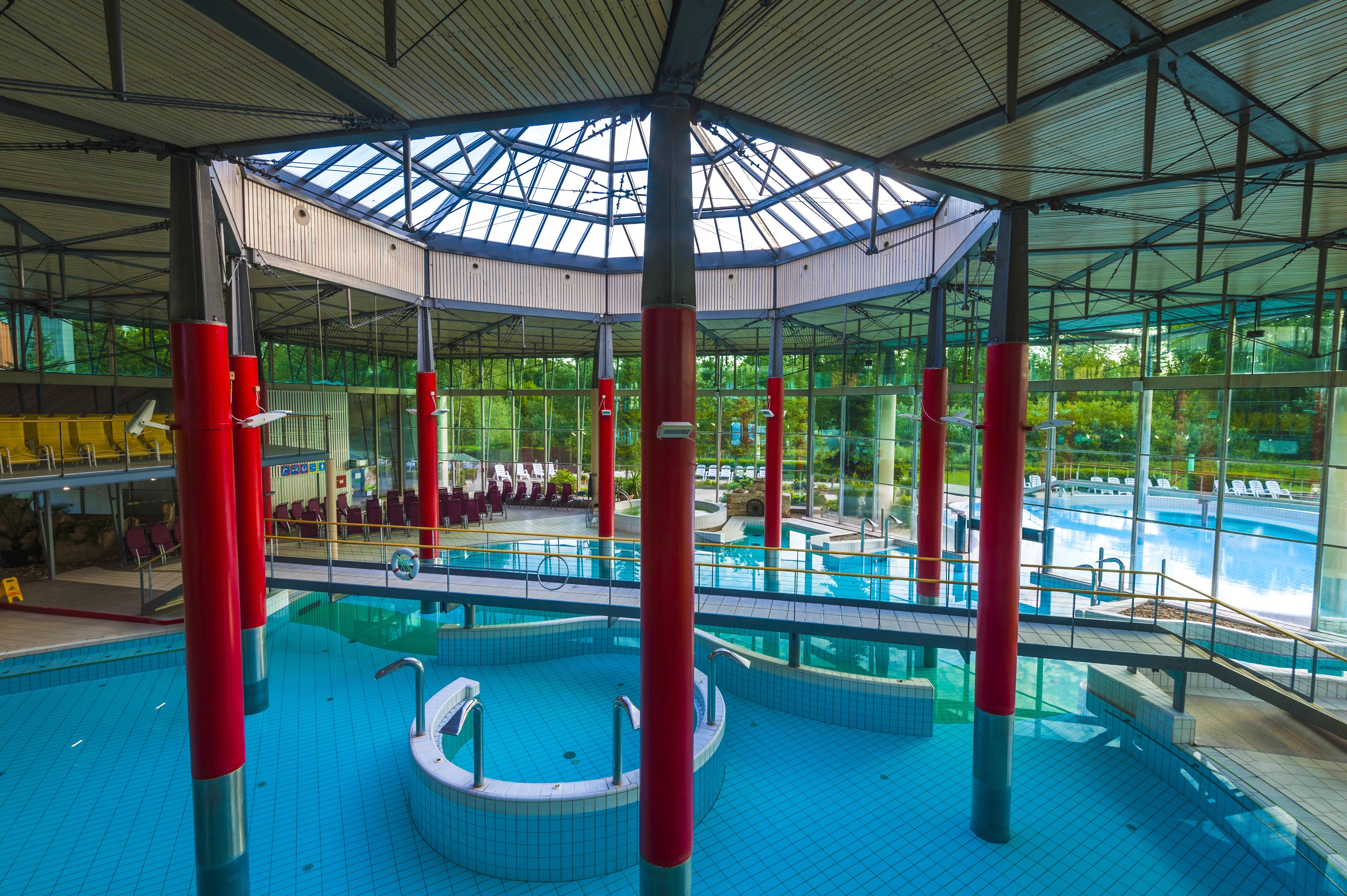 An indoor swimming pool with a glass ceiling, multiple lanes, and a sun deck area.