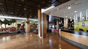 Ein Hotel-Empfangsbereich mit poliertem Marmorboden, einer Rezeption und einem großen Spiegel.