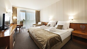 Ein Hotelzimmer mit einem großen Bett, einem Schreibtisch mit Fernseher, einem Sessel und einem Nachttisch mit Lampe.