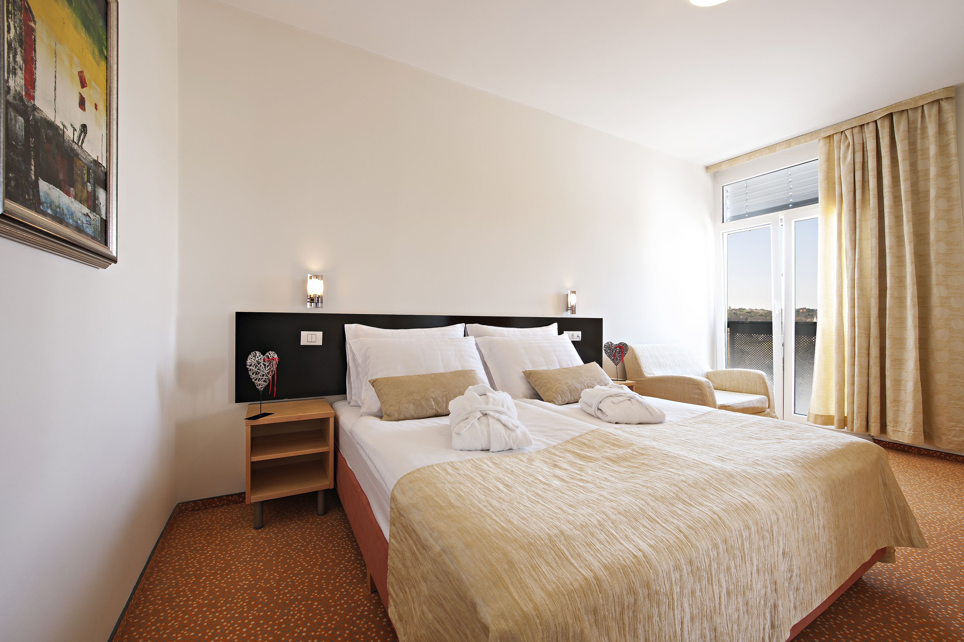 Habitación de hotel con una cama grande, una mesita de noche, un televisor montado en la pared y una ventana con cortinas.