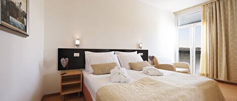 Habitación de hotel con una cama grande, una mesita de noche, un televisor montado en la pared y una ventana con cortinas.