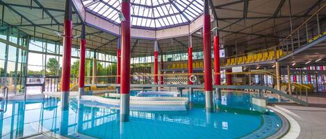 Une piscine intérieure dotée d’un toit en verre, de piliers rouges et d’un sol carrelé.