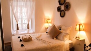 A neatly made bed with white linens, two bedside lamps, and a window with sheer curtains. - Riad Amra (Marrakech)