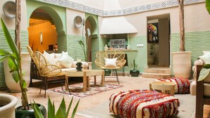 A cozy courtyard with wicker chairs, a sofa, and a dining area. There are potted plants and a large vase. - Riad Amra (Marrakech)