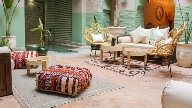 A cozy lounge area with wicker furniture, a patterned ottoman, and a decorative wall. - Riad Amra (Marrakech)