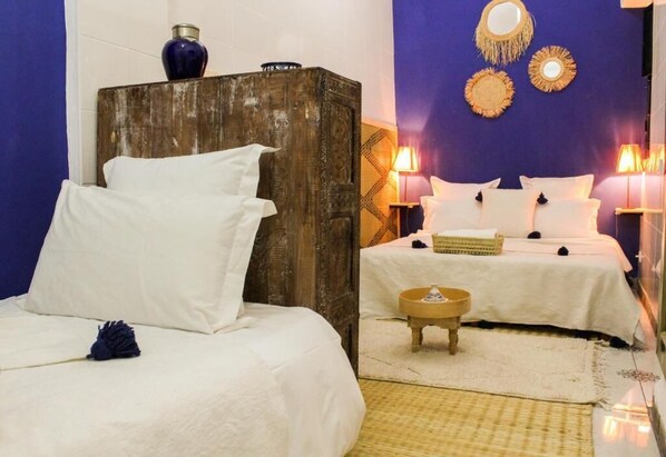 Una habitación con dos camas, cabecera de madera, una mesita redonda y decoración en las paredes.