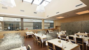 Un restaurante con varias mesas y sillas, ventanas amplias y un techo alto con tragaluces.