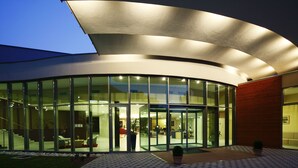 Un edificio moderno con grandes ventanales, techo curvo y un área de entrada bien iluminada.