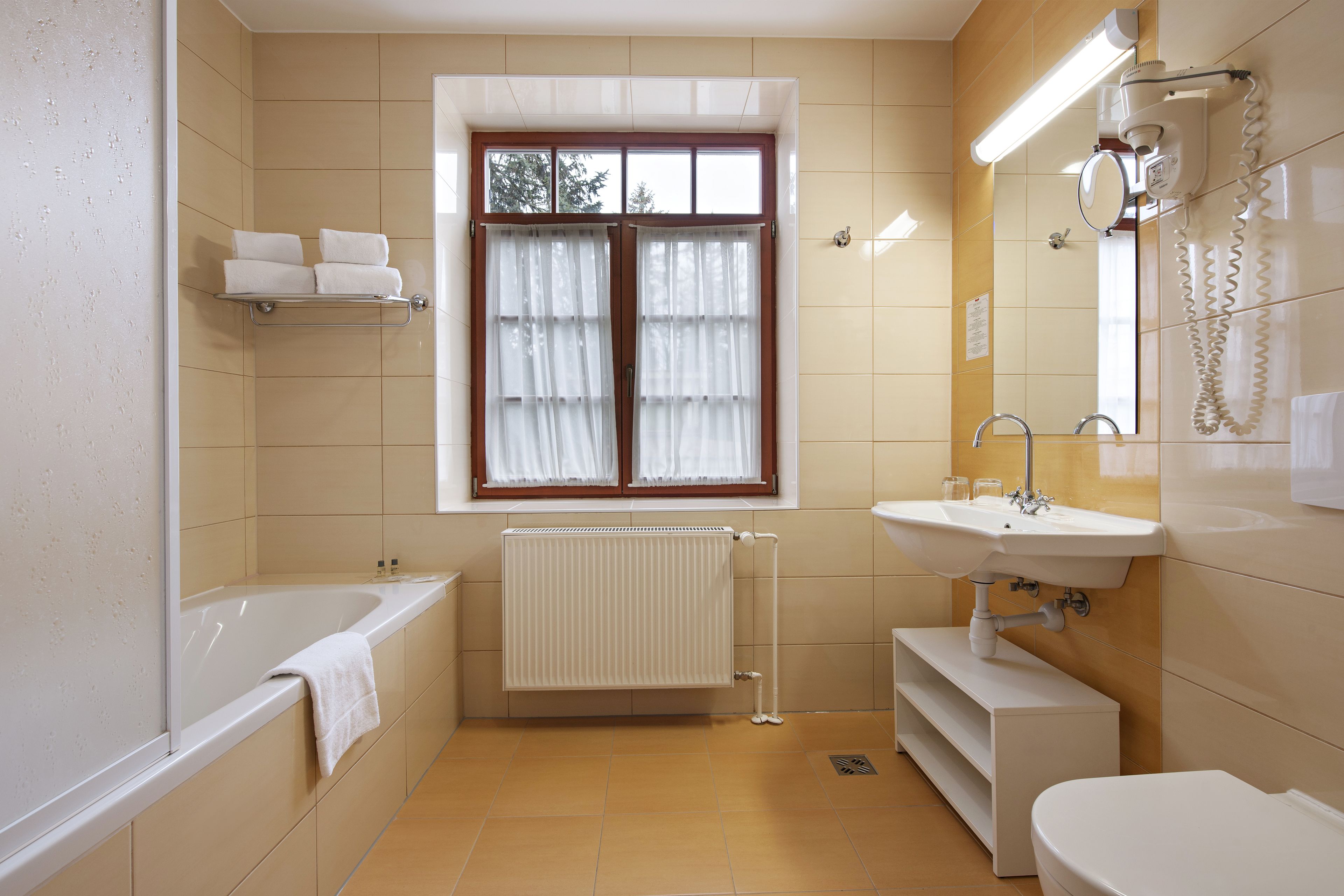 A bathroom with a bathtub, a toilet, a sink, and a window with curtains.