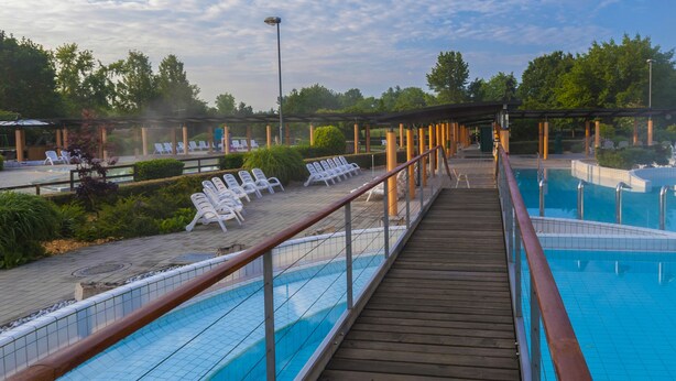 Una terraza de madera que da a una zona de piscina con sillones de descanso y un cielo azul despejado.