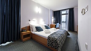 Habitación de hotel con cama, mesita de noche, lámpara y vistas al exterior a través de una ventana.