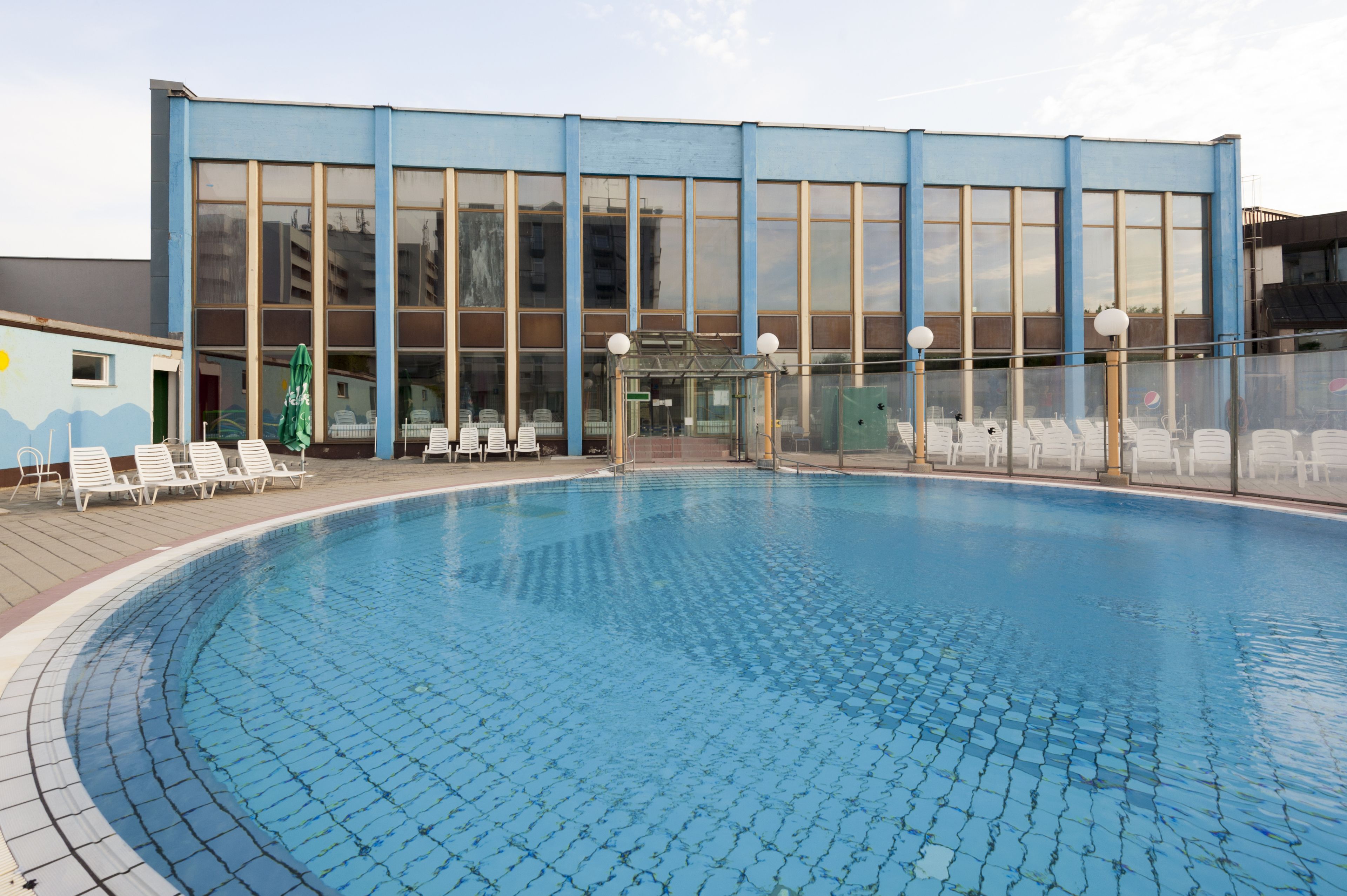 En swimmingpool med solstolar och en byggnad med stora fönster i bakgrunden.