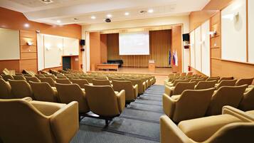 A conference room with rows of chairs, a podium, a screen, and flags.