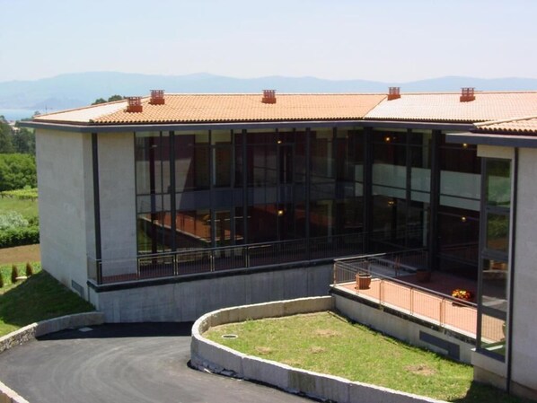 A modern building with large glass windows, a curved roof, and a landscaped area with a pathway. - Peregrina (Sanxenxo)
