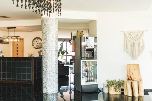 A lobby with a black tiled reception desk, a mosaic pillar, a vending machine, and a macrame wall hanging. - Peregrina (Sanxenxo)