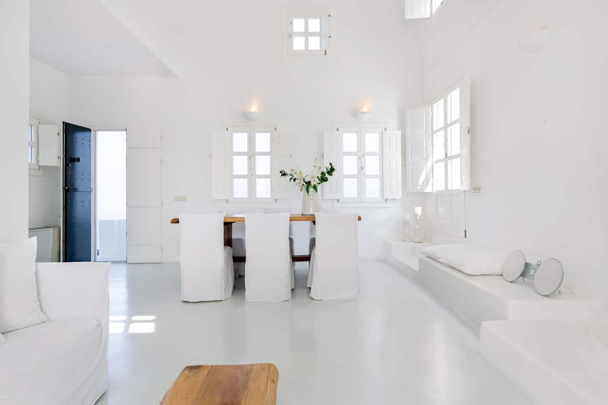 A spacious, modern living room with a wooden coffee table, white sofas, and a dining area with chairs and a table.