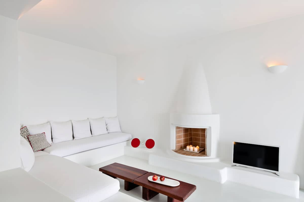 A modern living room with a white sofa, a wooden coffee table, a fireplace, and a flat-screen TV.