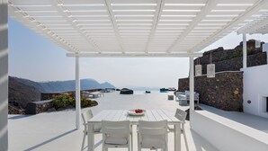 Un espace extérieur aménagé avec des sièges blancs, offrant une vue sur la mer et les montagnes.
